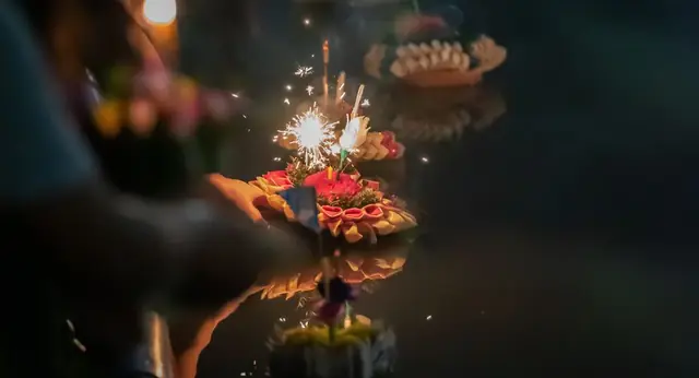 A krathong with a lit sparkler on dark water