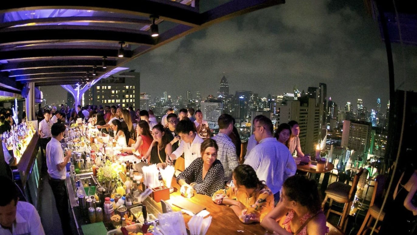 The crowded bar at Above Eleven on the 33rd floor, the Sukhumvit skyline lit up behind it