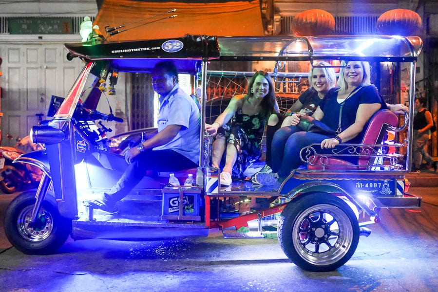 Three guests in Bangkok Food Tours' lit-up tuk-tuk at night