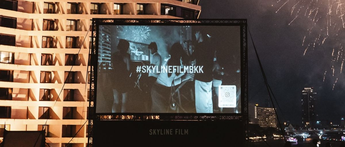 Skyline Film’s rooftop screen at River City Bangkok at night, with fireworks over the river behind it