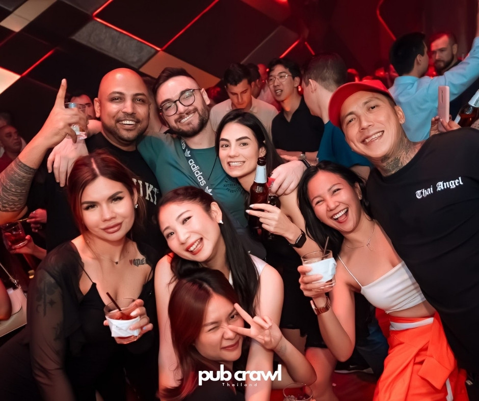 A group on Pub Crawls Thailand's Sukhumvit Soi 11 crawl, drinks raised, in a club lit red
