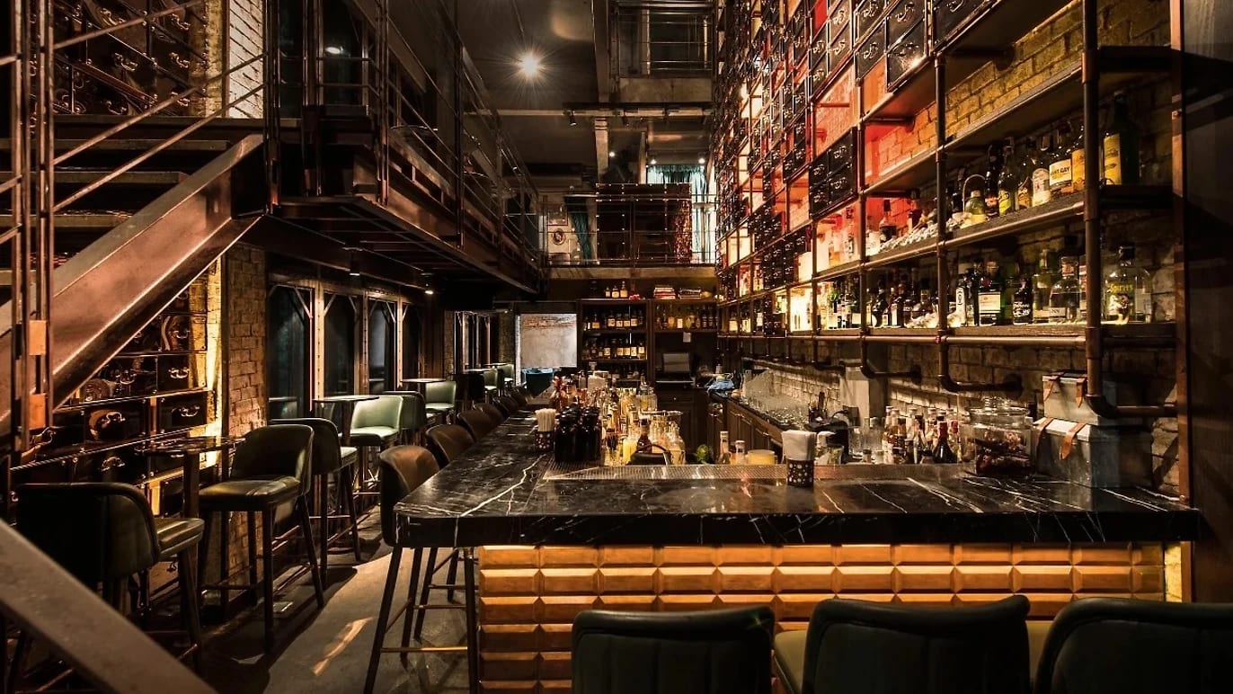 Rabbit Hole's long marble bar under a mezzanine, bottles lit on the back wall