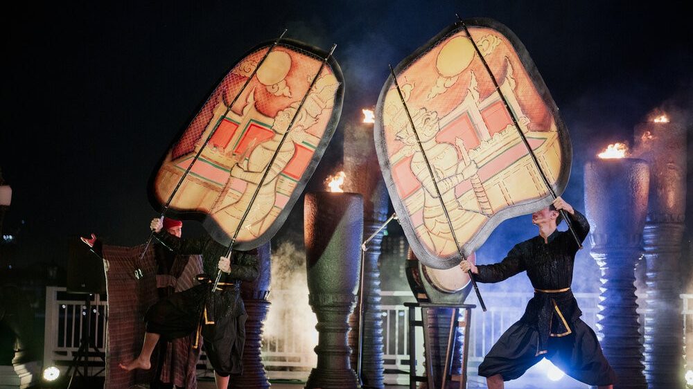 Dancers holding large painted Nang Yai shadow puppets by firelight at Sala Lakorn