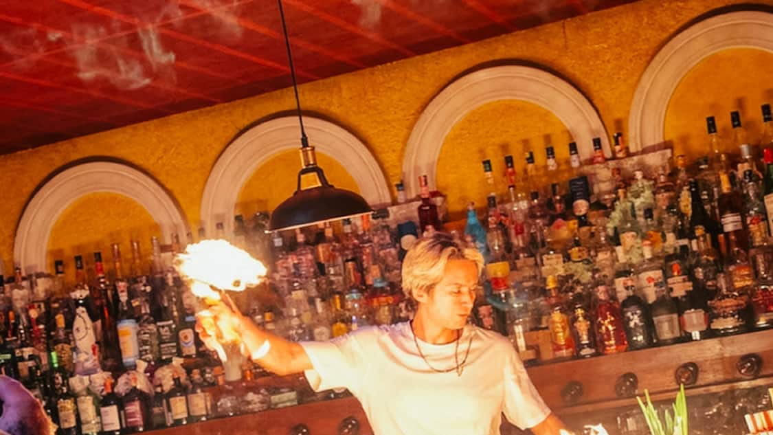 A bartender at Homie Bar lighting the bar top, flames along the counter