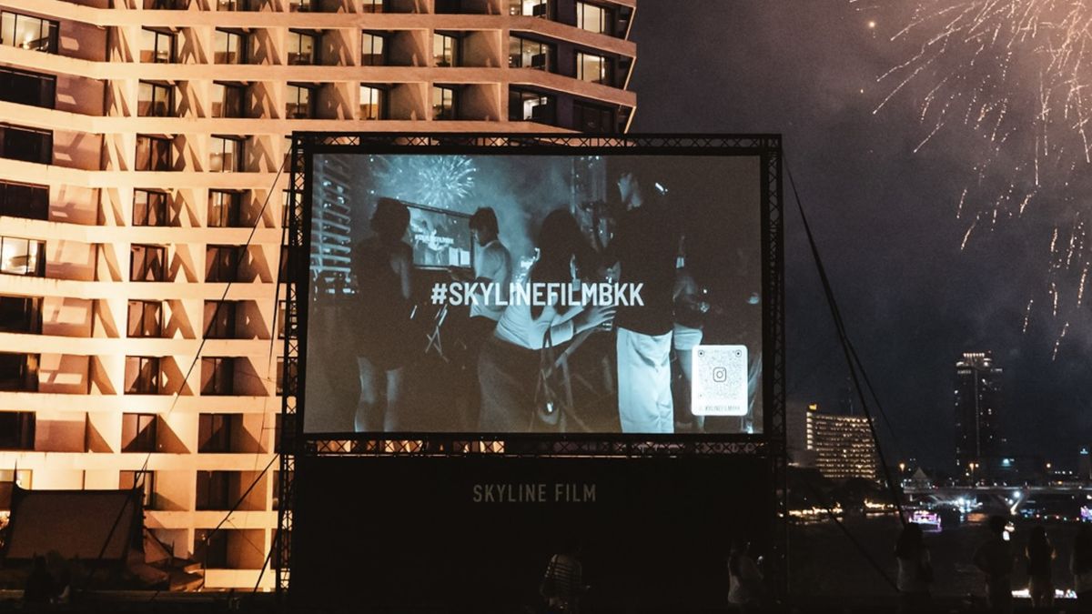 Skyline Film's rooftop screen at River City Bangkok at night, with fireworks over the river behind it