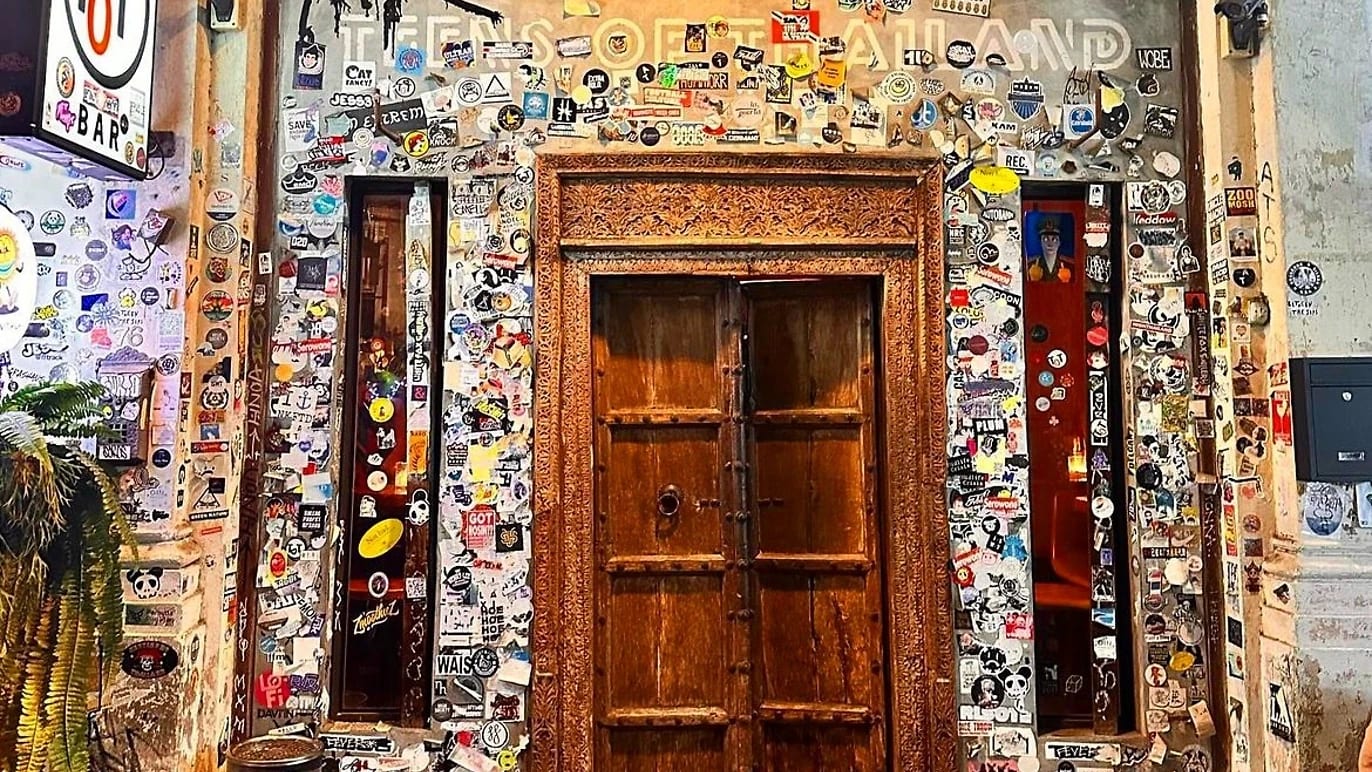 The carved wooden door of Teens of Thailand on Soi Nana, framed by a wall of stickers