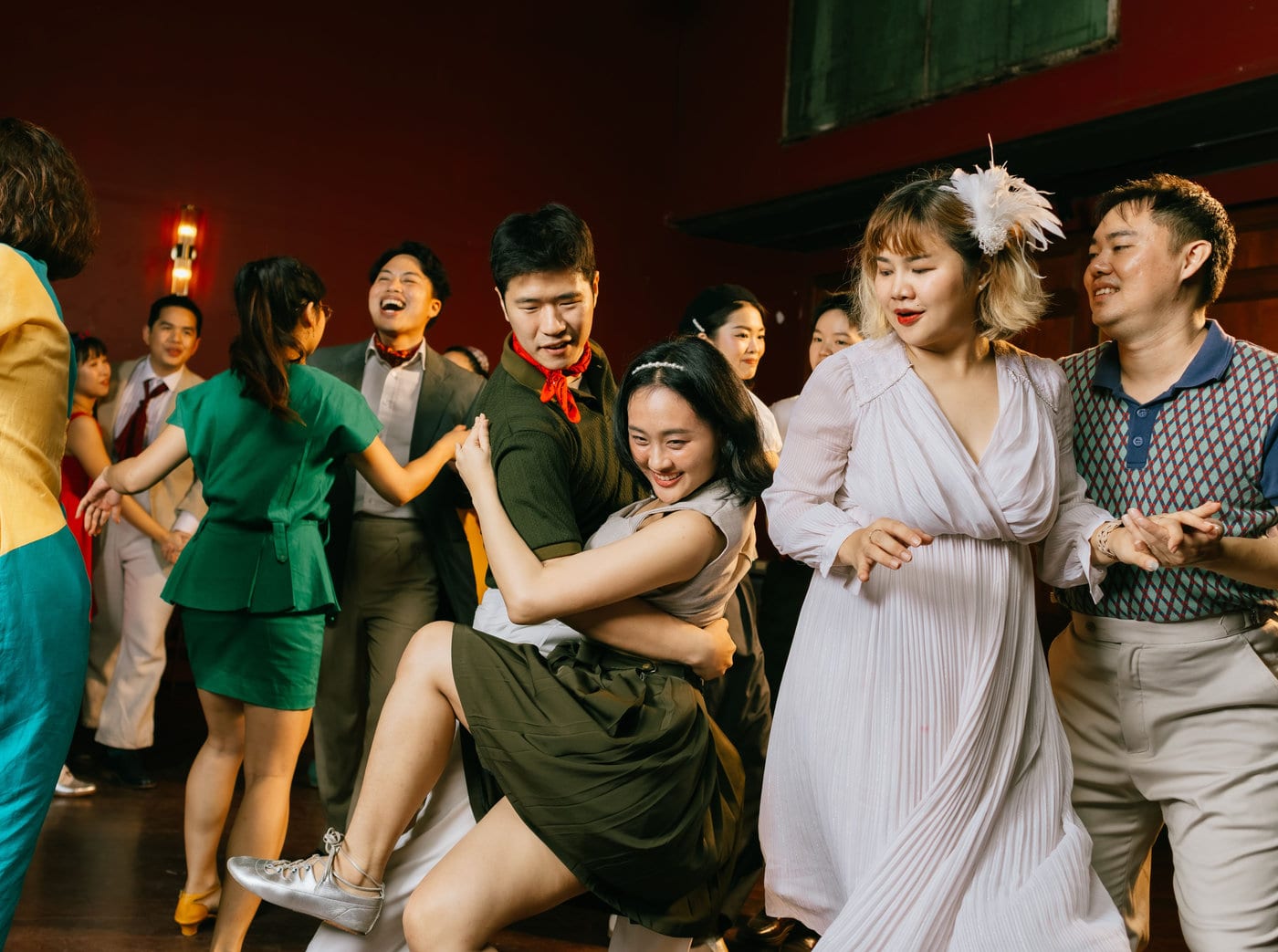Couples swing dancing in vintage dress on The Hop's red-walled floor in Silom