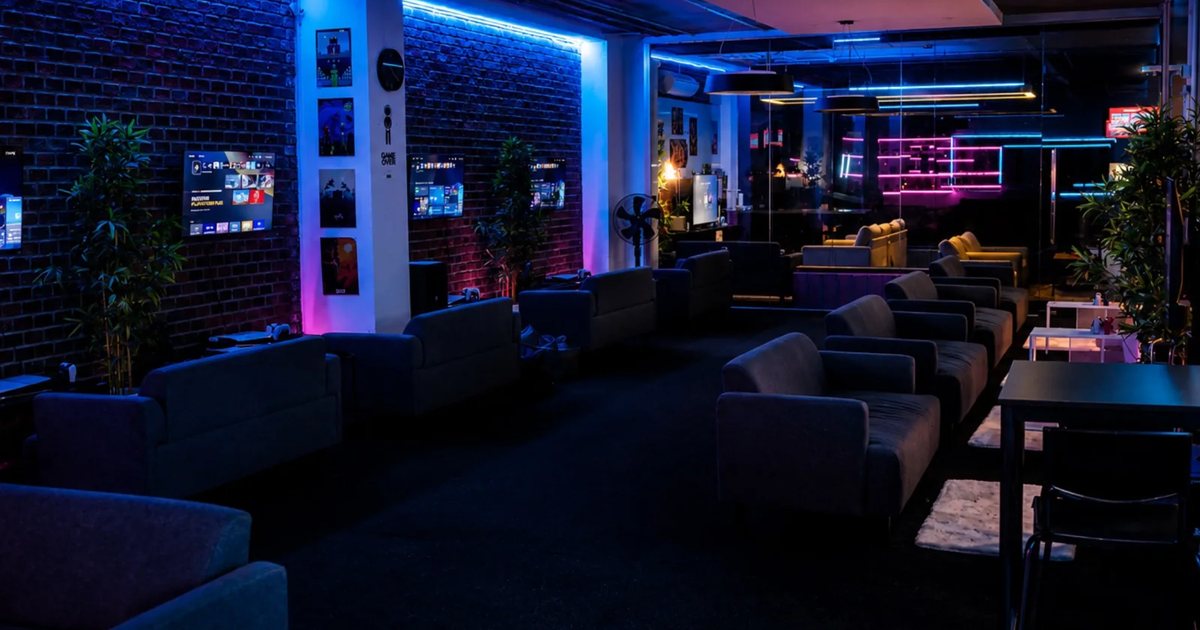 Sofas facing rows of wall-mounted screens in Bamboo Gaming Center's lounge, lit blue and pink